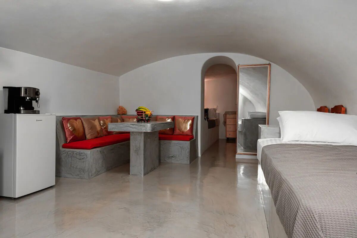 A modern, compact room with a bed, a small table, and a seating area with cushions.