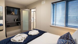 Una habitación de hotel con cama, armario, zona de ducha y ventana con persianas.