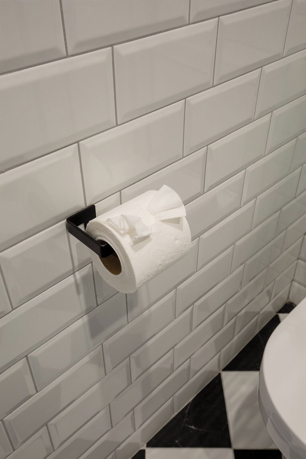 A toilet paper holder mounted on a tiled wall in a bathroom.