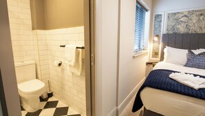 Un baño con inodoro, ducha y cama con cabecero.
