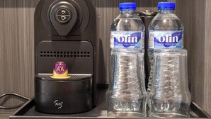 Un minibar con una cafetera, dos botellas de agua irlandesa y una variedad de cartones de leche y zumo.