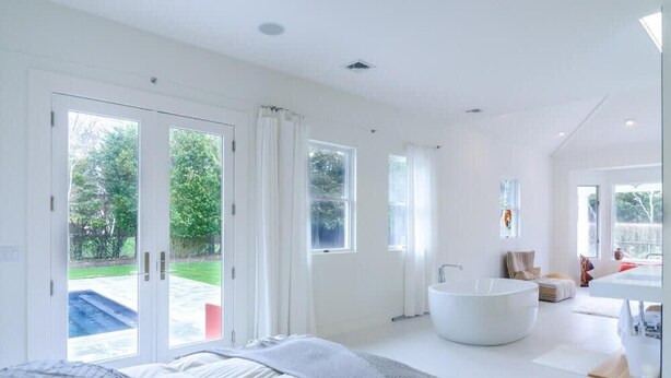 A modern bedroom with a large bed, a freestanding bathtub, and a view of a garden through the glass doors. - West Hamptons Zen Retreat (Westhampton)