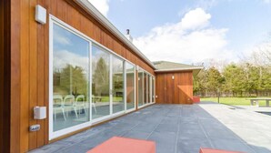 A modern building with large glass sliding doors, a flat roof, and a patio area with red seating. - West Hamptons Zen Retreat (Westhampton)
