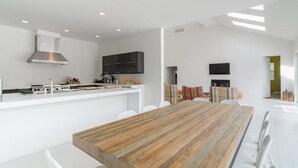 A modern kitchen with white cabinetry, a wooden dining table, and a built-in stove. - West Hamptons Zen Retreat (Westhampton)