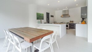 A modern kitchen with white cabinetry, a wooden dining table, and white chairs. - West Hamptons Zen Retreat (Westhampton)