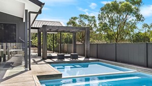 Una piscina con cubierta de madera, una pérgola y mobiliario de exterior.
