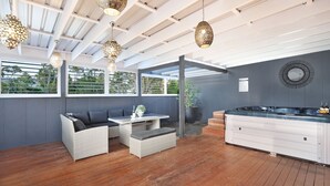 Un área de cocina exterior moderna con estufa integrada, barra y zona de estar con mobiliario de mimbre.