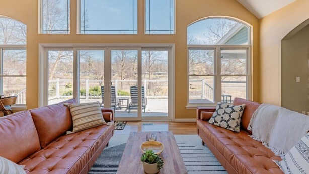 A spacious living room with leather sofas, a coffee table, and large windows offering a view of the outdoors.
