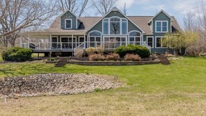 A large, two-story house with a covered porch and a stone retaining wall in front.