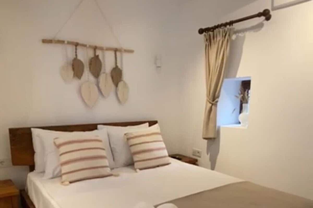 Ein ordentlich bezogenes Bett mit beiger Bettdecke und Kissen, ein Holz-Kopfbrett und ein kleiner Nachttisch mit einer Lampe.