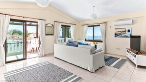 Ein geräumiges Wohnzimmer mit Sofa, Fernseher und einem Balkon mit Vorhängen.