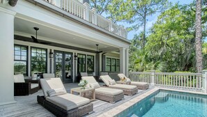 A covered outdoor area with a pool, wicker furniture, and a balcony with railings.