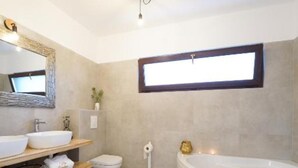 Une salle de bain moderne avec une baignoire sur pieds, un grand miroir et une étagère où sont rangées les serviettes et les articles de toilette.