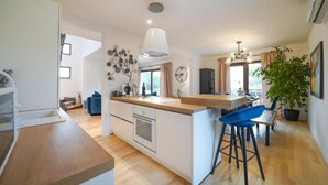 A modern kitchen with a central island, bar stools, and a dining area with a view. - Villa Sunshine (Sukosan)