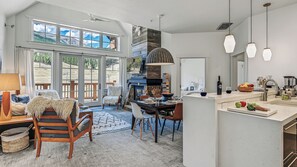 Un vaste espace de vie comprenant un coin salon avec cheminée, une table à manger et une vue sur l’extérieur.