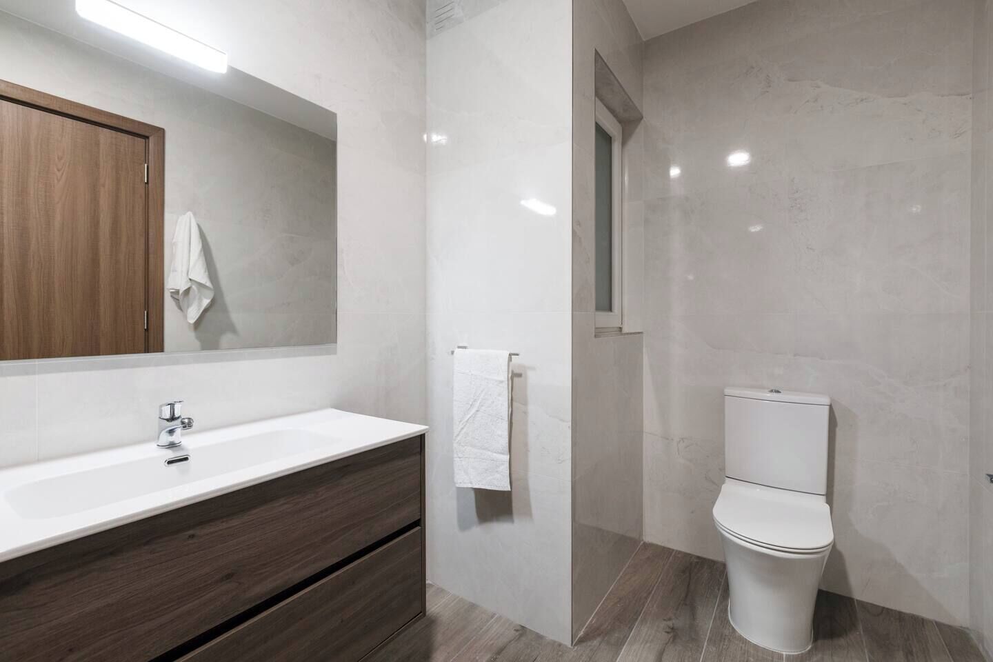 A modern bathroom with a white sink, dark wooden vanity, a large mirror, and a white toilet.