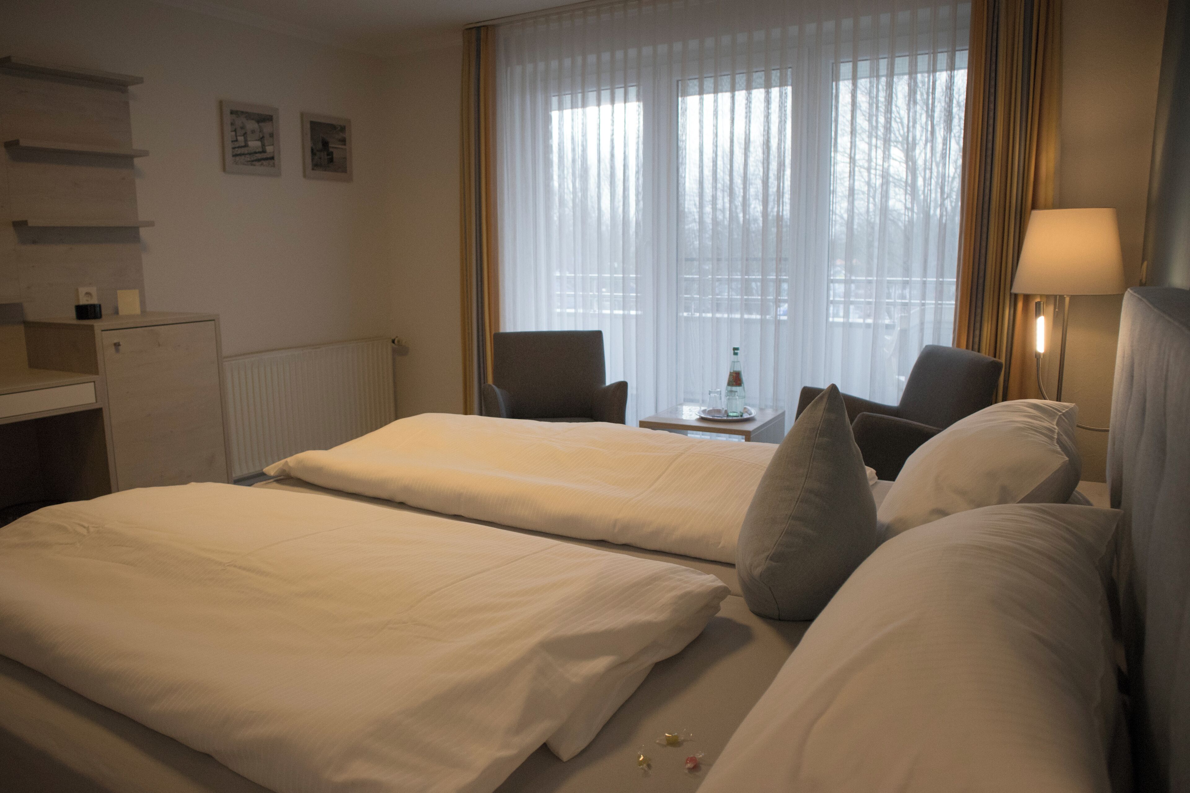 A hotel room with two beds, a desk, a chair, and a window with curtains.