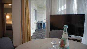 Una habitación de hotel con zona de comedor, televisión y una botella de agua sobre la mesa.