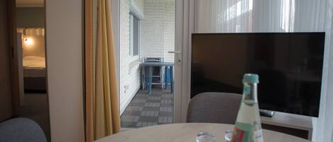 Una habitación de hotel con zona de comedor, televisión y una botella de agua sobre la mesa.