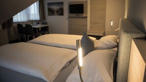 A hotel room with two beds, a desk, a chair, and a TV on the wall.