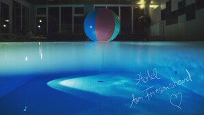 A swimming pool with a large ball in the center, a lounge area with chairs, and a sign that reads "Hotel am Friesenhand."