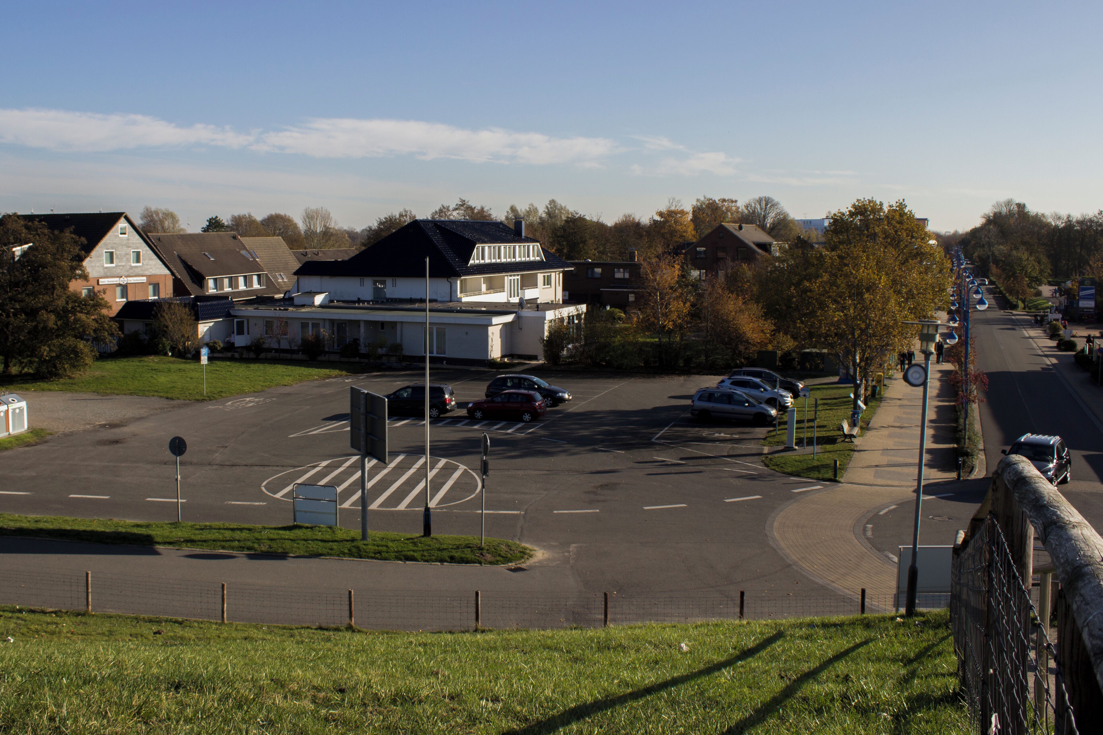 A parking lot with multiple cars, a pedestrian crossing, and a road leading to a residential area with houses.