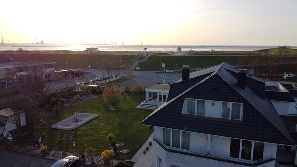 A residential area with a house featuring a sloped roof and large windows, a well-maintained lawn, and a view of the sea in the background. - Hotel Am Friesenstrand (Butjadingen)