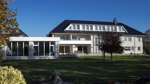 A two-story building with a large balcony, a covered patio, and a well-maintained lawn.