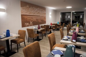 A modern dining area with tables and chairs, a large painting on the wall, and a view into the dining area through glass doors. - Hotel Am Friesenstrand (Butjadingen)
