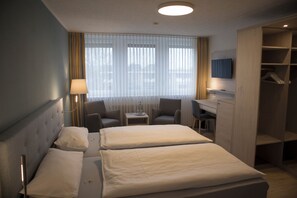 A hotel room with two beds, a desk, a chair, a TV, and a wardrobe. - Hotel Am Friesenstrand (Butjadingen)