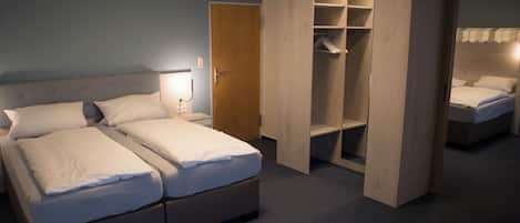 A bedroom with a double bed, a wooden wardrobe, and a nightstand with a lamp.