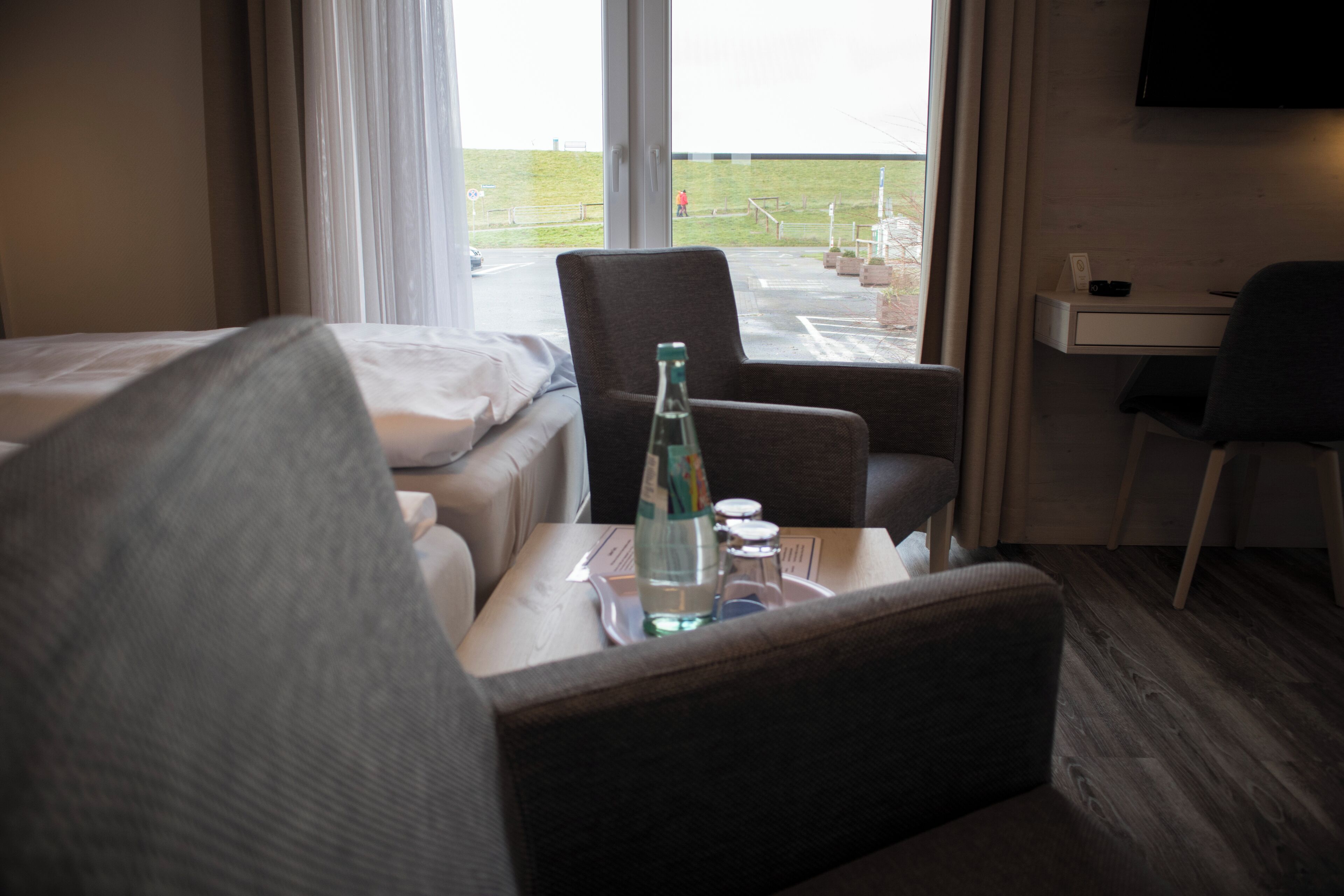 Een hotelkamer met een bed, een stoel, een klein tafeltje met een fles en glazen, en een televisie aan de muur.
