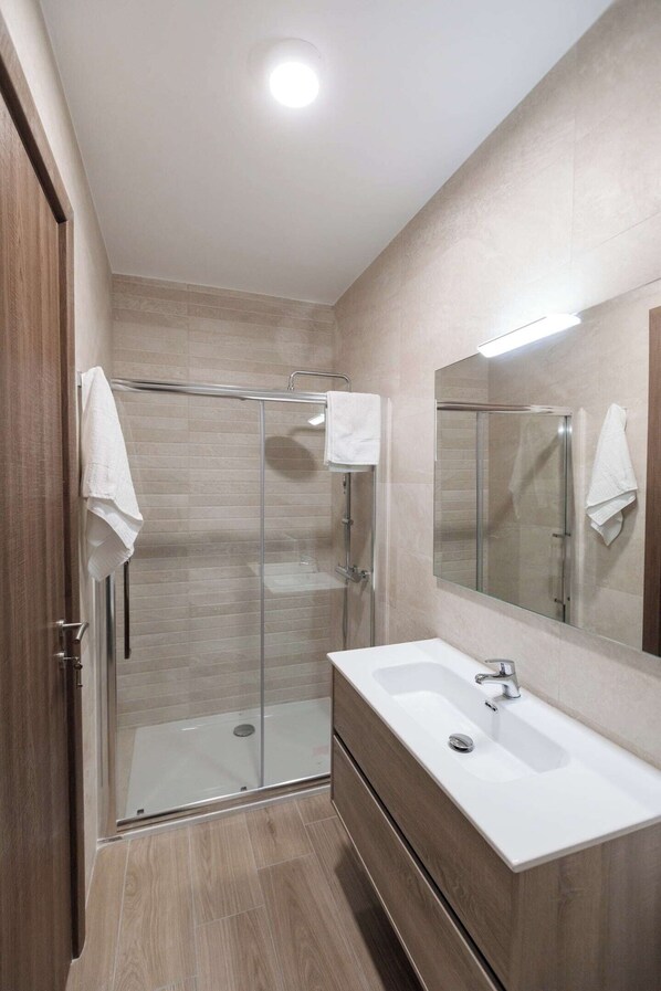 A modern bathroom with a glass shower enclosure, a large mirror, and a wooden vanity.