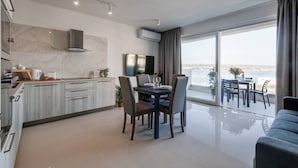 A modern kitchen with marble countertops, a dining area with a table and chairs, and a balcony with a view of the sea.