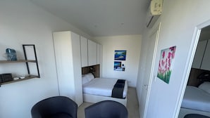 Une pièce de taille modeste comprenant un lit, deux fauteuils, une petite table et une armoire.