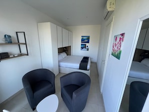 A compact room with a bed, two armchairs, a small table, and a wardrobe.