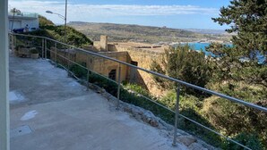 Une vue sur la côte, avec un ciel dégagé, un chemin pavé et une rambarde donnant sur la mer.