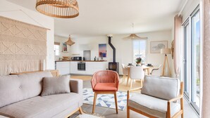 Uma sala de estar moderna com um sofá, duas poltronas, um espaço de jantar e uma cozinha ao fundo.