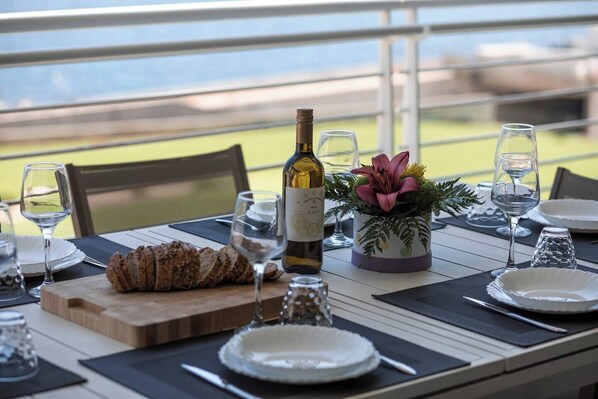Une table à manger dressée avec des assiettes, des verres, une bouteille de vin, un pain et un arrangement floral décoratif.