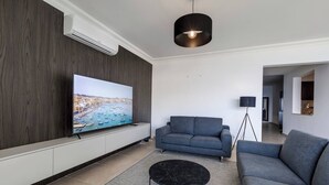 Un salon moderne avec un téléviseur à écran plat, des canapés gris, une table basse noire et un luminaire suspendu.