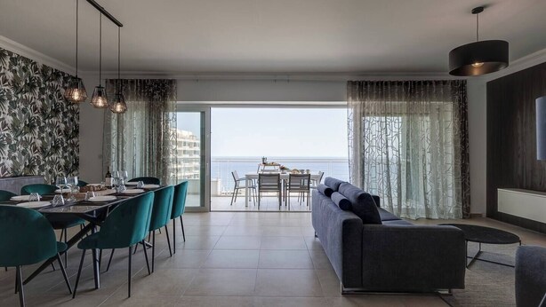 Un salon moderne avec un coin repas, de grandes fenêtres et une vue sur la mer.