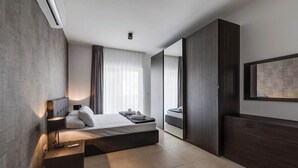 Una habitación de hotel moderna con una cama grande, una mesita de noche, un armario y un ventanal amplio.