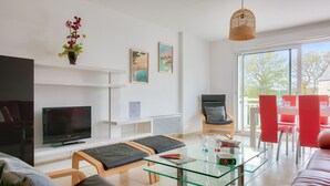 A modern living room with a flat-screen TV, glass coffee table, comfortable seating, and a large window offering a view of the outdoors. - Close to beaches and shops, flat for 4 (Fouesnant)