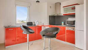 A modern kitchen with red cabinets, two black bar stools, a window with a view, and a Bosch microwave. - Close to beaches and shops, flat for 4 (Fouesnant)