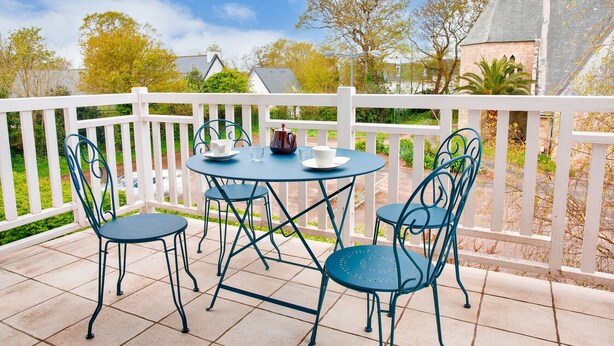 A patio with a round table and four chairs, a white fence, and a view of houses and trees. - Close to beaches and shops, flat for 4 (Fouesnant)