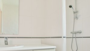 A bathroom with a white sink, a mirror, and a shower with a handheld showerhead. - Close to beaches and shops, flat for 4 (Fouesnant)
