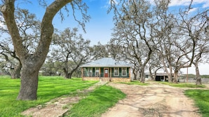 A rustic cabin with a stone foundation and a metal roof, surrounded by mature trees and a dirt path leading to it. - Expansive Hill Country Ranch w/ Pool Access on 2,001 Acres (Johnson City)