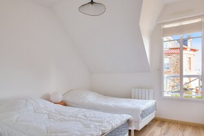 Un dormitorio con dos camas, una ventana con vista a un edificio y una lámpara en el techo.
