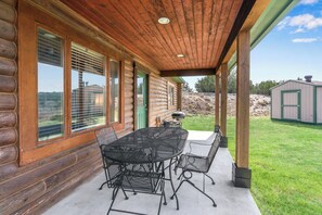A covered patio with a metal table and chairs, large windows, and a view of the surrounding landscape. - Lighthouse Hill Ranch - Log Home - situated on 2001 acres! (Johnson City)
