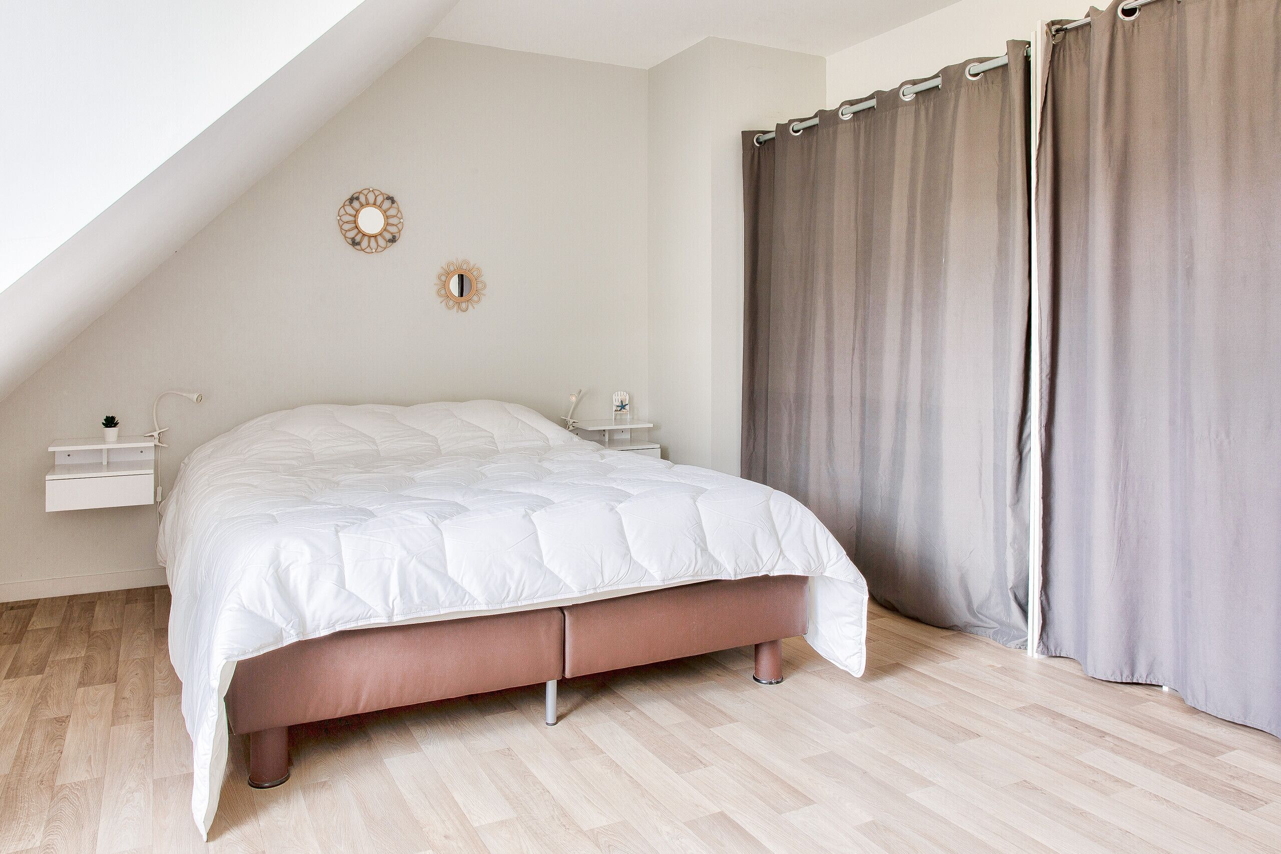 A bedroom with a bed, bedside tables, a mirror, and a window with curtains.